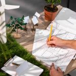 Architect designing eco-friendly building with wind turbine and solar panel models on a desk with plant decoration